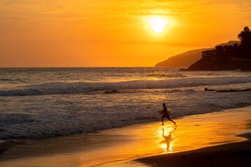 Fototapeta na wymiar A view of a surfer during a colorful sunset on the beach in El Zonte in El Salvador. Surf City.