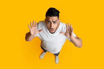 Top view of confused middle eastern guy raising hands up