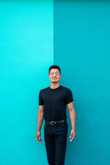 latino man in his 30s poses with black clothes and glasses on turquoise wall