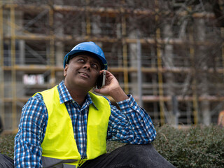 Indian or Somali engineer with safety jacket and helmet talking on mobile phone on construction site