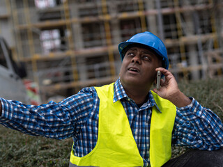 Indian or Somali engineer with safety jacket and helmet talking on mobile phone on construction site