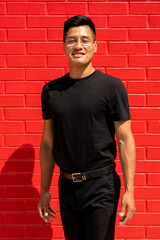 30 year old latin man in black clothes and glasses on red brick background