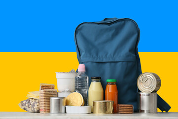 Backpack and different products against flag of Ukraine. Humanitarian aid for Ukrainian refugees...
