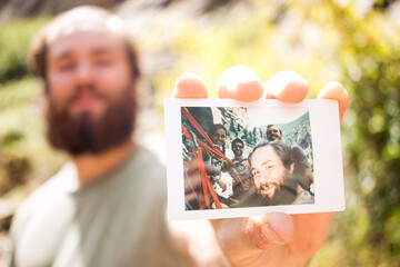 Friendly man holding up and showing polaroid of climbing friends