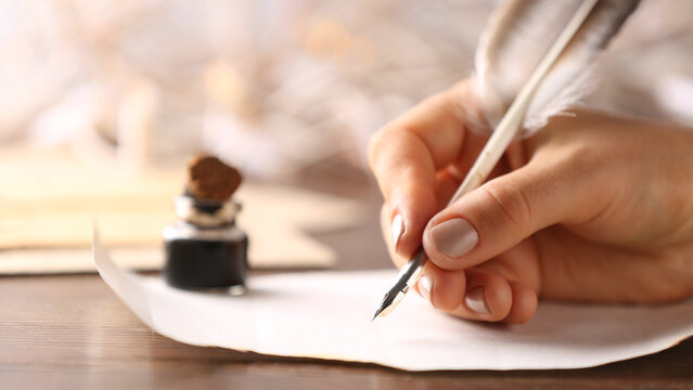 Woman writing in ink on paper sheet at table, closeup