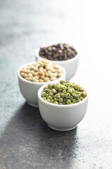 Three different types of pepper spice. Green, white and black peppercorn in bowls.