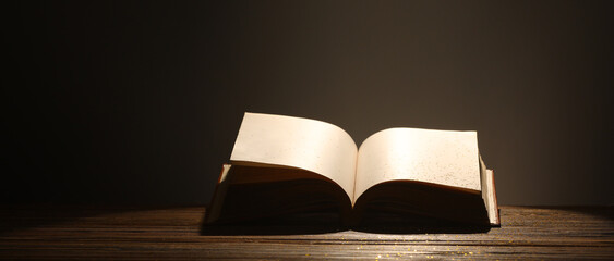 Open book on wooden table against dark background