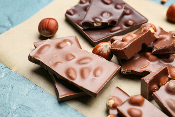 Pieces of tasty chocolate with nuts on parchment