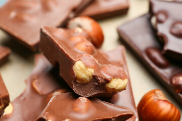 Pieces of tasty chocolate with hazelnuts on table, closeup