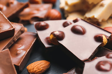 Pieces of tasty chocolate with nuts on dark background, closeup