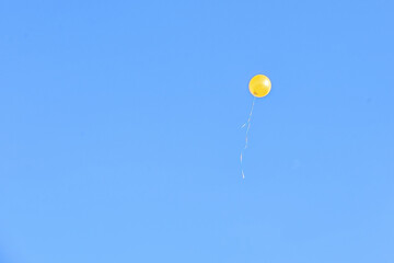 on a clear bright blue sky, a yellow balloon flies up
