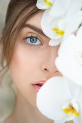 Obraz na płótnie Canvas Beautiful young woman's face with perfect skin and makeup covers part of her face by tropical orchid. Portrait of beauty model with flower. Spa, skincare and wellness. Close up, selective focus