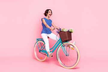 Full length photo of impressed millennial brunette lady ride bicycle wear blouse pants shoes isolated on pink background