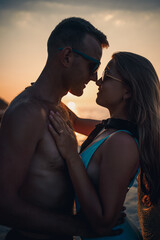Beautiful couple in love on the background of the sunset by the sea. Young woman and man hugging by the sea at sunset