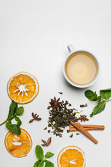 Top view of cups of tea near mint, spices and dry orange slices on white background.