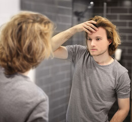 young man looking in the mirror,combing his hair,looking at problems on face.