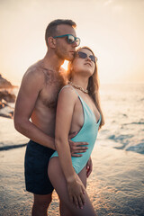 A loving couple walks along the beach by the sea. Young family at sunset by the Mediterranean Sea. Vacation concept. A woman in a swimsuit and a man in shorts at sunset by the sea. Selective focus.