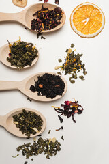 Top view of dry tea in spoons near orange slice on white background.