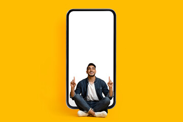 Excited middle eastern guy pointing at smartphone, mockup