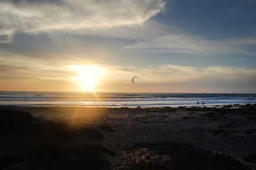 A kiteboarder and two surfers enjoying their time at Jalama Beach, during sunset over the Pacific Ocean, in Santa Barbara County, California.