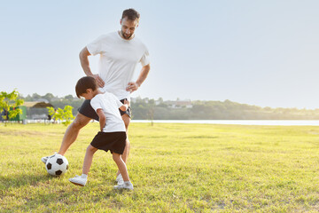 Little boy playing soccer with his father on field