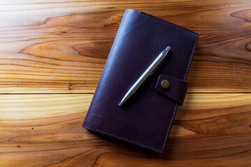 Overhead view of metal pen and leather journal on beautiful wood table