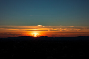 Sunset sunrise at city with bright colorful dramatic sky and dark ground with silhouettes of mountains