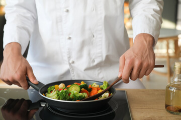 Male chef with spatula frying tasty vegetables in kitchen, closeup