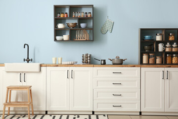 Interior of stylish kitchen with white counters, shelves and supplies