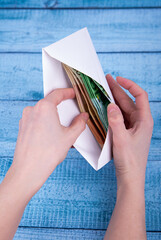 Hands holding an open envelope with money on a blue background