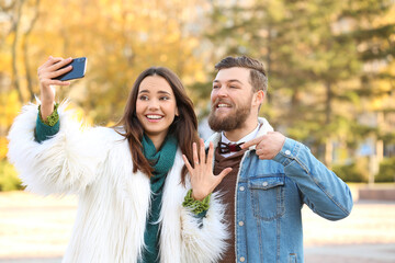 Happy young woman with ring and her fiance taking selfie after marriage proposal in park