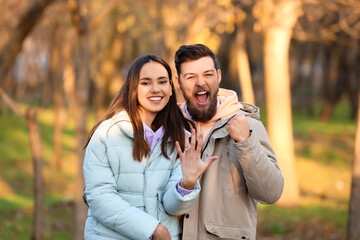 Happy young woman with engagement ring and her fiance in forest