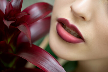 Red lips of beautiful young woman with tropical scarlet red flower. Close up, selective focus.