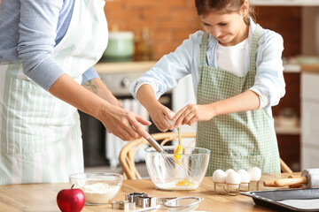 Little girl with her grandmother breaking egg into bowl in kitchen