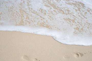 Sandy shore with footprints, an oncoming sea wave. Natural background, travel and tourism
