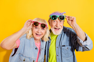 Portrait of attractive amazed cheerful grey-haired family touching specs having fun isolated over bright yellow color background