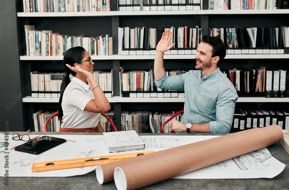 Poster we did it again. cropped shot of two cheerful young architects high fiving each other while working 