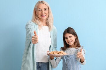 Mature woman and her little granddaughter with cookies on blue background