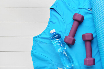 Stylish dumbbells, t-shirt and bottle of water on light wooden background