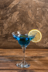 Blue cocktail in glass on wooden surface on textured stone background.