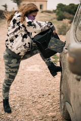 woman in camouflage clothes pouring fuel on a car fuel tank from a jerrycan