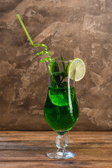 Glass of green cocktail with drinking straw on wooden surface on textured stone background.