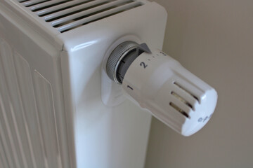 Detail on metal central heating with a control part for regulating temperature. The heating is white as well is the wall in the background.