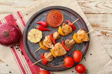 Plate of grilled chicken skewers with vegetables on white wooden background
