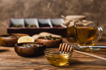 Bowl with honey near blurred tea on wooden surface on brown background.