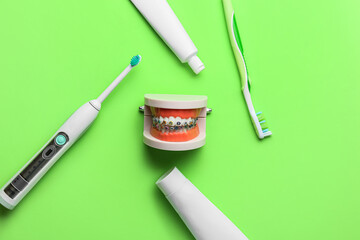 Model of jaw with dental braces, tooth brushes and paste on green background