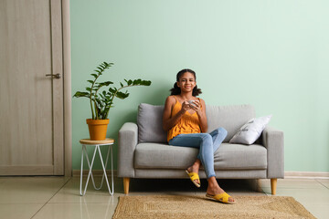 African-American teenage girl drinking tea while sitting on sofa at home