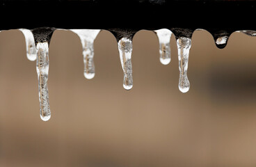 frozen water droplets hanging under a gritty metal rail with cracks and inclusions visible, on a...