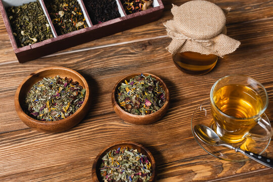 High angle view of dry tea in bowls and jar with honey on wooden surface.