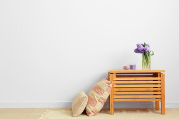 Vase with hyacinth flowers, candles on table and pillows near white wall in room
